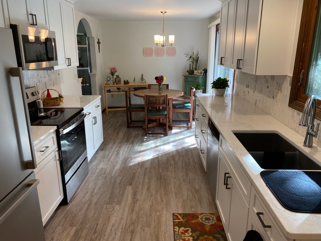 After image of kitchen standing in the corner looking across the room at the updated fridge, stove, and cabinets